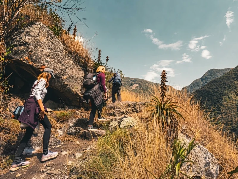 Hikers walking along a dirt trail past green agricultural fields on the Inca Trail