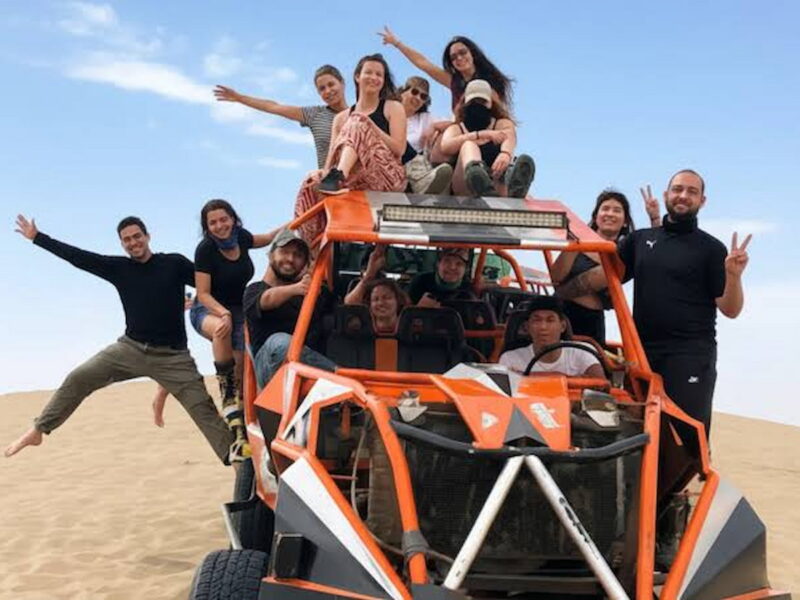 Dune buggy crossing the Huacachina dunes with travellers sandboarding