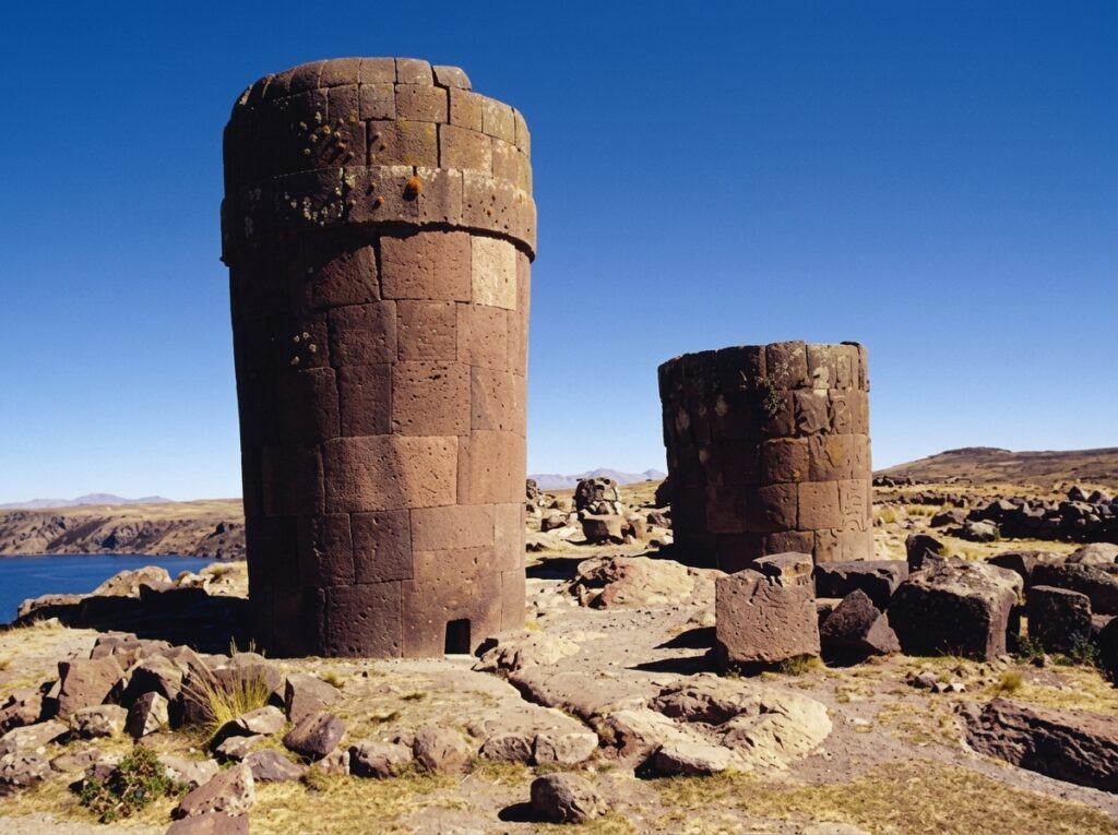 Two pre-Inca chullpa funerary towers standing on the altiplano at Sillustani, with Umayo Lagoon behind them, near Puno, Peru