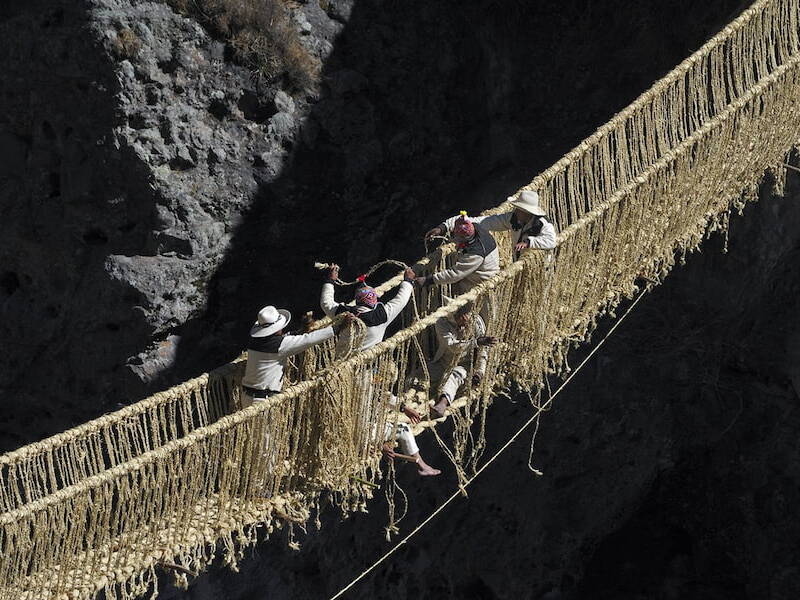 Comuneros con sombrero y chullo trenzan las sogas de ichu del puente Q'eswachaka sobre el río Apurímac