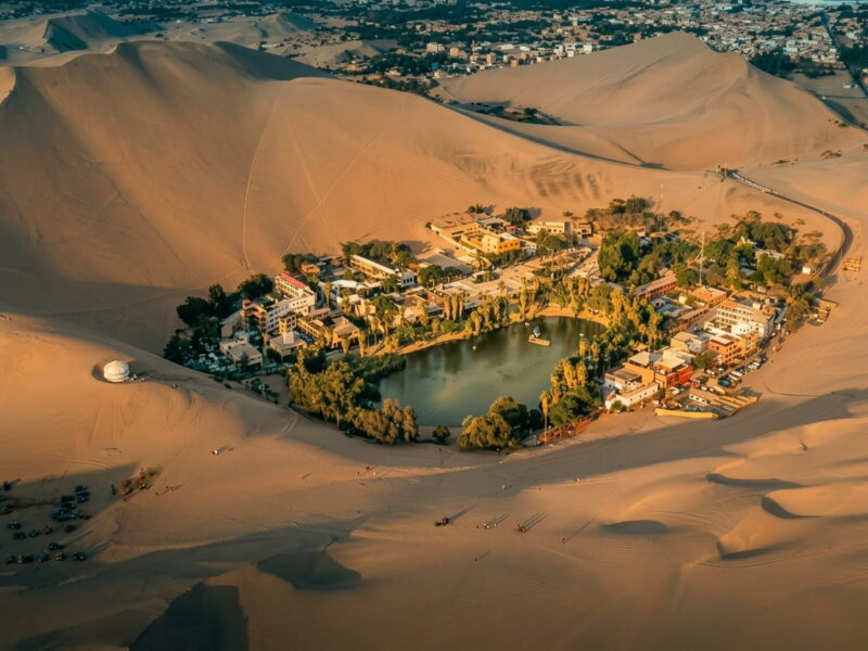 Vista aérea del Oasis de Huacachina rodeado por altas dunas de arena en Ica.