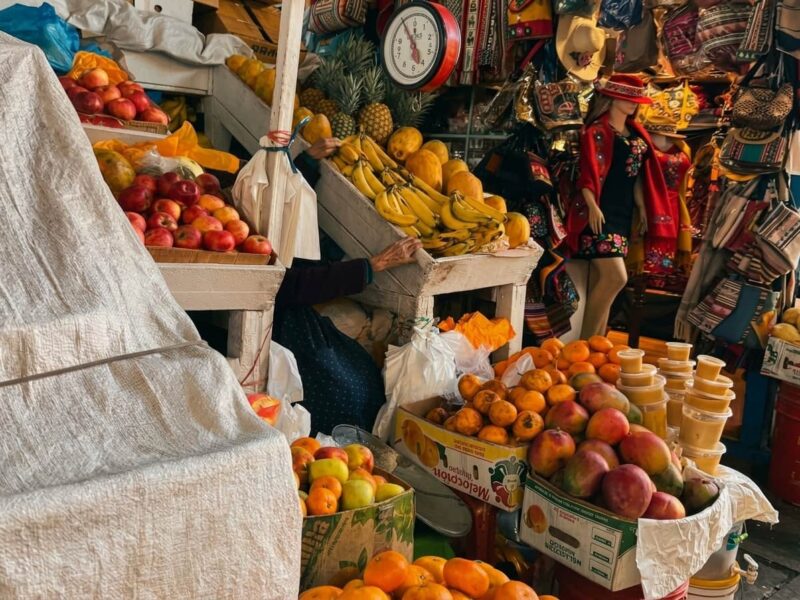 Puestos de venta coloridos con frutas frescas y textiles andinos dentro del Mercado San Pedro en Cusco.