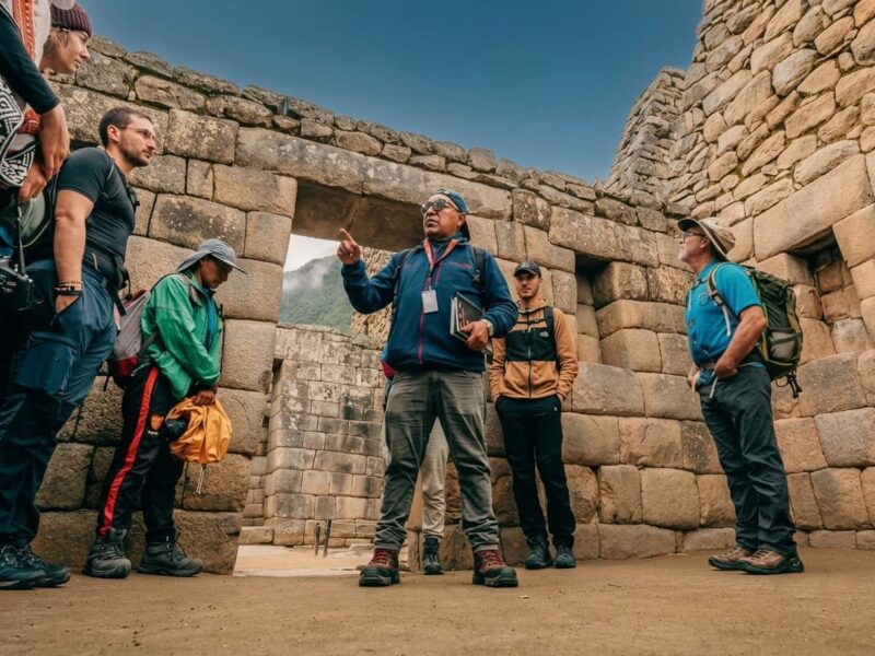 Guía profesional explicando a un grupo de turistas junto a las terrazas de piedra de Machu Picchu.