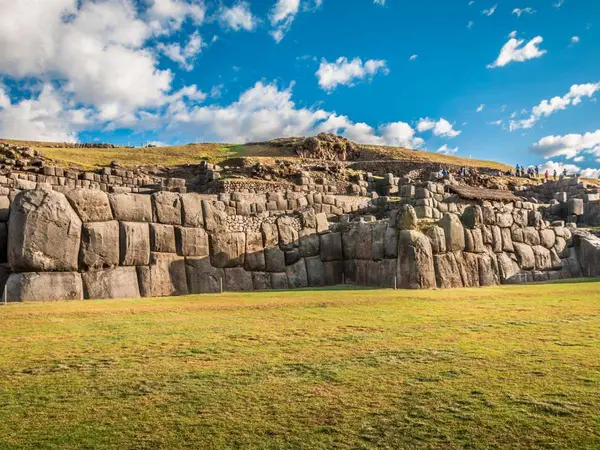 Muro inca de Sacsayhuamán hecho con piedras enormes perfectamente encajadas, sobre una explanada de césped bajo un cielo azul con nubes
