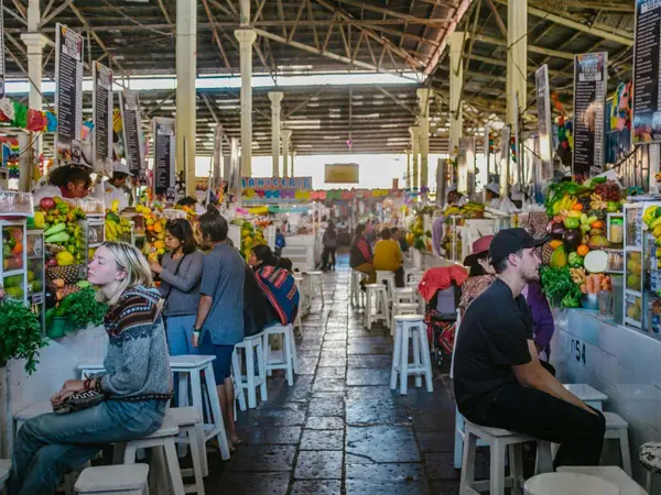 Pasillo del Mercado de San Pedro en Cusco con puestos de jugos llenos de frutas y viajeros sentados en taburetes