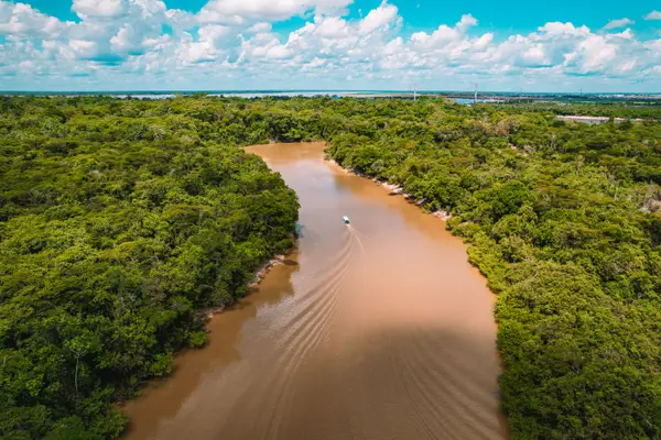 Vista aérea de un río amazónico de aguas marrones con un bote navegando entre la selva y un puente al fondo