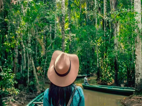 Viajera con sombrero frente a un canal de la selva con canoas de madera amarradas en la orilla