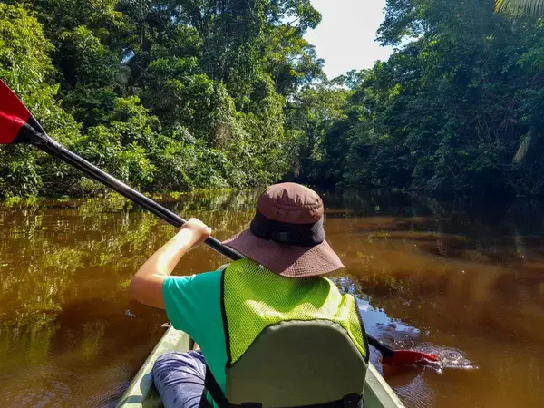 Viajera con sombrero remando en kayak por un río de aguas marrones rodeado de selva
