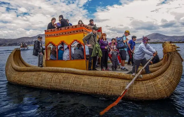Turistas a bordo de una balsa de totora con proa en forma de cabeza de puma en el Lago Titicaca, junto a las islas de los Uros