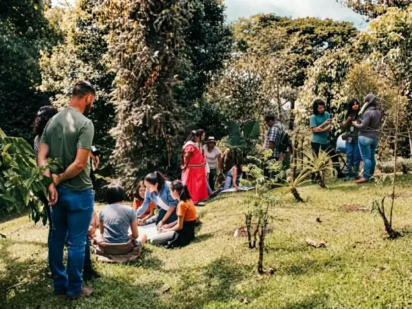 Grupo de viajeros reunidos al aire libre en un jardín con árboles y plantas jóvenes, escuchando una explicación