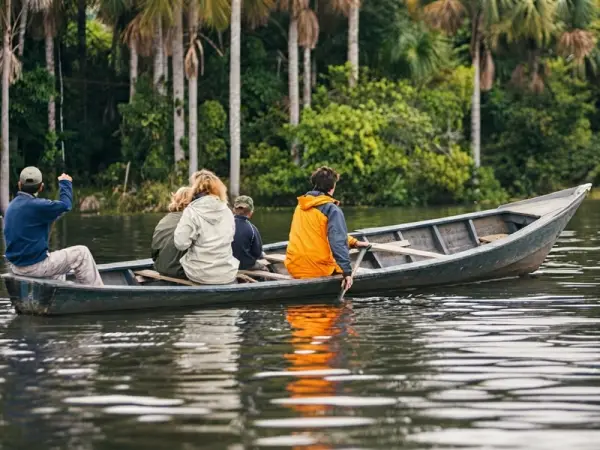 Viajeros con chalecos salvavidas en un bote de madera a remo sobre las aguas tranquilas del Lago Sandoval
