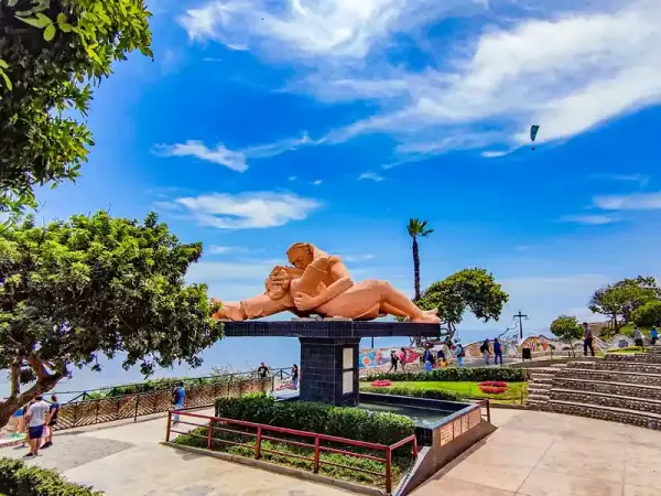 Escultura de una pareja besándose en el Parque del Amor de Miraflores, con palmeras y el cielo azul de Lima