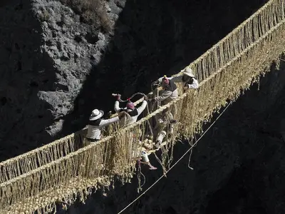 Comuneros con sombrero y chullo trenzan las sogas de ichu del puente Q'eswachaka sobre el río Apurímac
