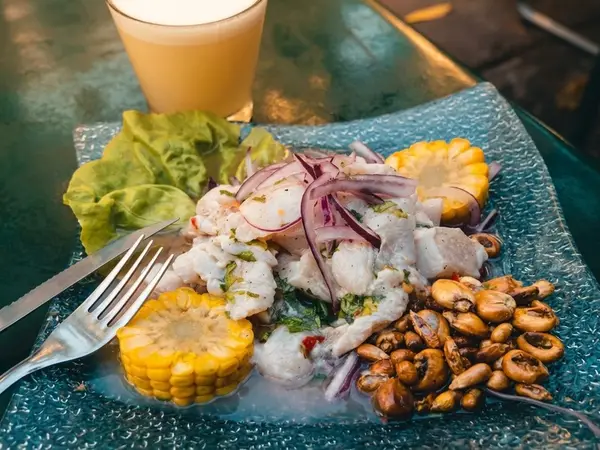 Ceviche de pescado con cebolla morada, choclo, cancha y lechuga, servido junto a un vaso de jugo en un restaurante de Lima
