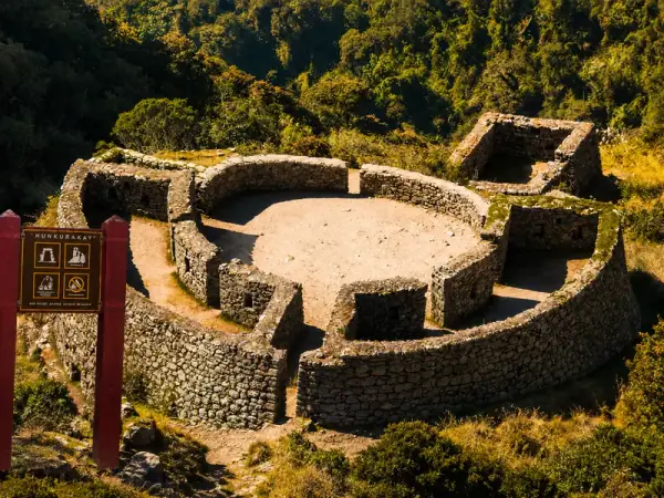 Round stone walls and inner courtyard of the Runkuracay ruin on the Inca Trail, with a site information sign