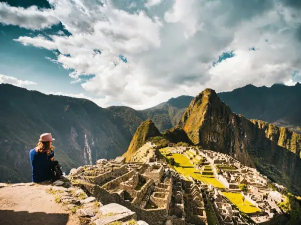 Traveller sitting on a rock above Machu Picchu, looking at the city and Huayna Picchu under a big sky