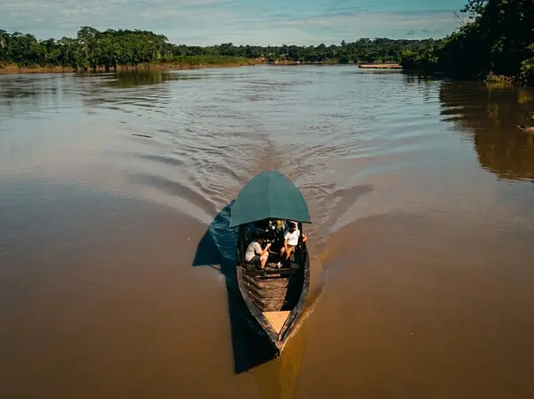 Bote de madera con viajeros navegando por el río Tambopata entre paredes de selva amazónica