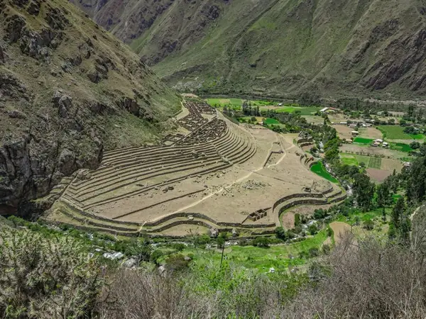 Curved Inca terraces of Patallacta on the valley floor, seen from the trail above with green fields beside the river