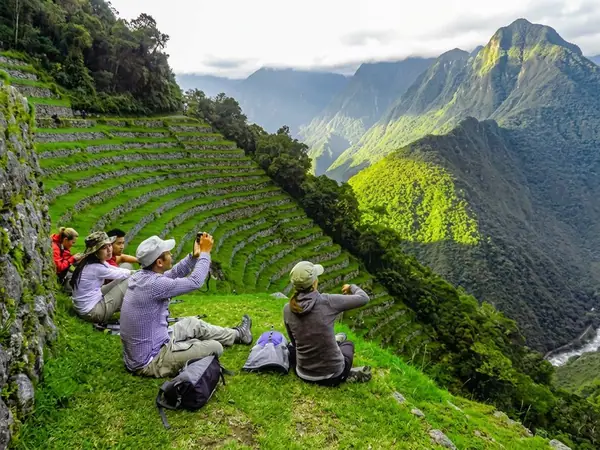 Hikers resting on the green terraces of Wiñay Wayna on the Inca Trail with cloudy mountains behind