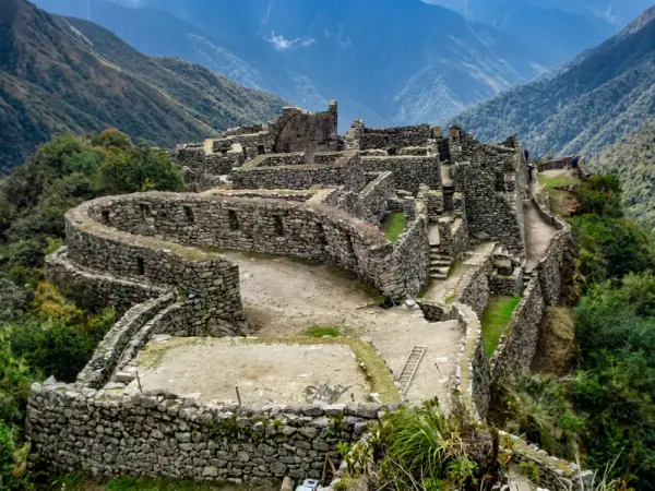 Curved stone walls and rooms of Sayacmarca built on a rocky spur above the forested valley on the Inca Trail