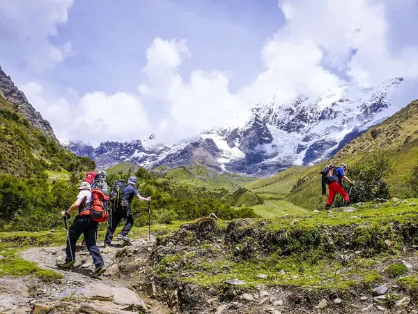 Hikers with trekking poles on the trail to Humantay Lake with snow-capped peaks ahead