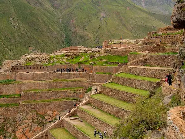 Visitors climbing the stepped stone terraces of the Ollantaytambo archaeological site, with green mountains behind